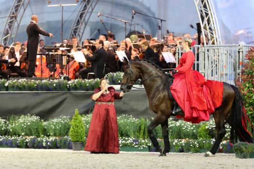 Foto: Helen Langehanenberg im Sattel von Rohjuwel. Es singt Kathy Kelly, im HIntergrund das Sinfonieorchester Aachen, dirigiert von Generalmusikdirektor Kazem Abdullah. - Fotograf: CHIO Aachen/Andraes Steindl
