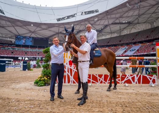 Foto: Felix Magath im Sattel von „Let’s go“. Als Grooms assistieren Ludger Beerbaum (rechts) und Michael Mronz - Fotograf: Longines Beijing Equestrian Masters/ Arnd Bronkhorst