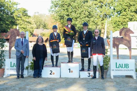 Foto: Die neuen Deutschen Meister der Amateur-Springreiter (v.l. Silber: Veronika Müller, Gold: Christin Lehrfeld, Bronze: Thomas Miesner), Richter und Titelsponsor Malte Laub (ganz re.) gratulieren - Fotograf: Buerstätte